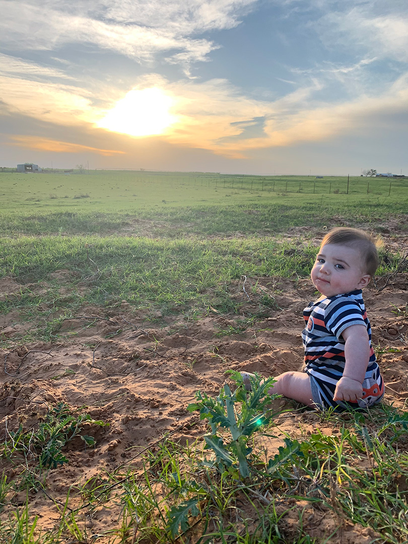 baby sitting in a field with the sun setting behind him